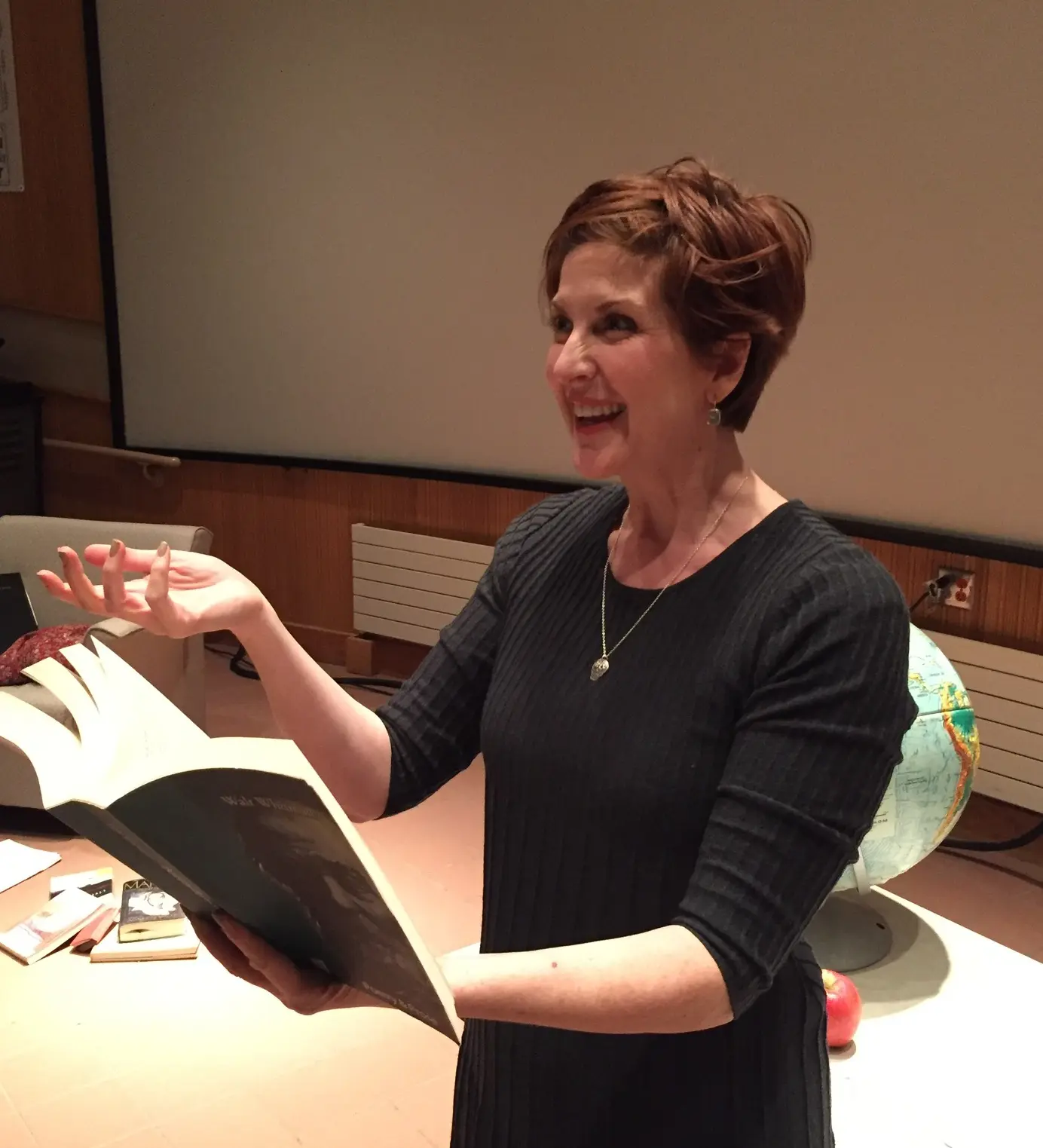 Woman smiling while reading large book aloud.