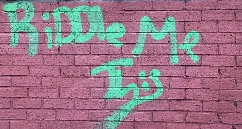 Riddle Me This" spray-painted on wall