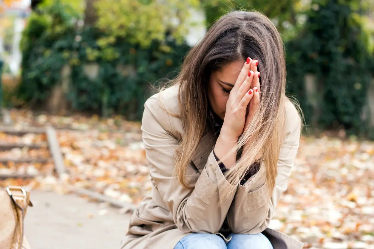 Woman sitting outdoors with hands together