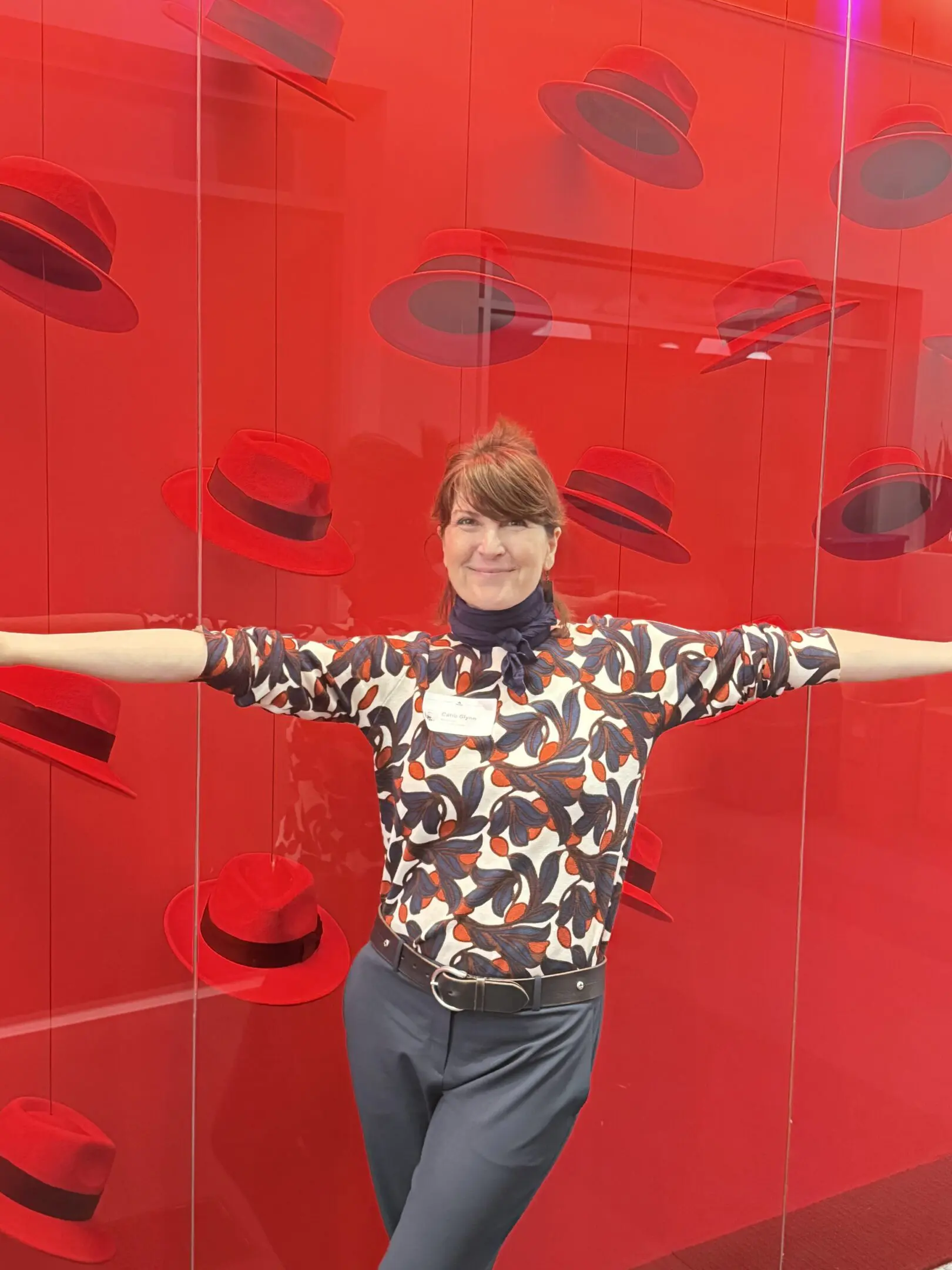 Person posing with red hats on wall.