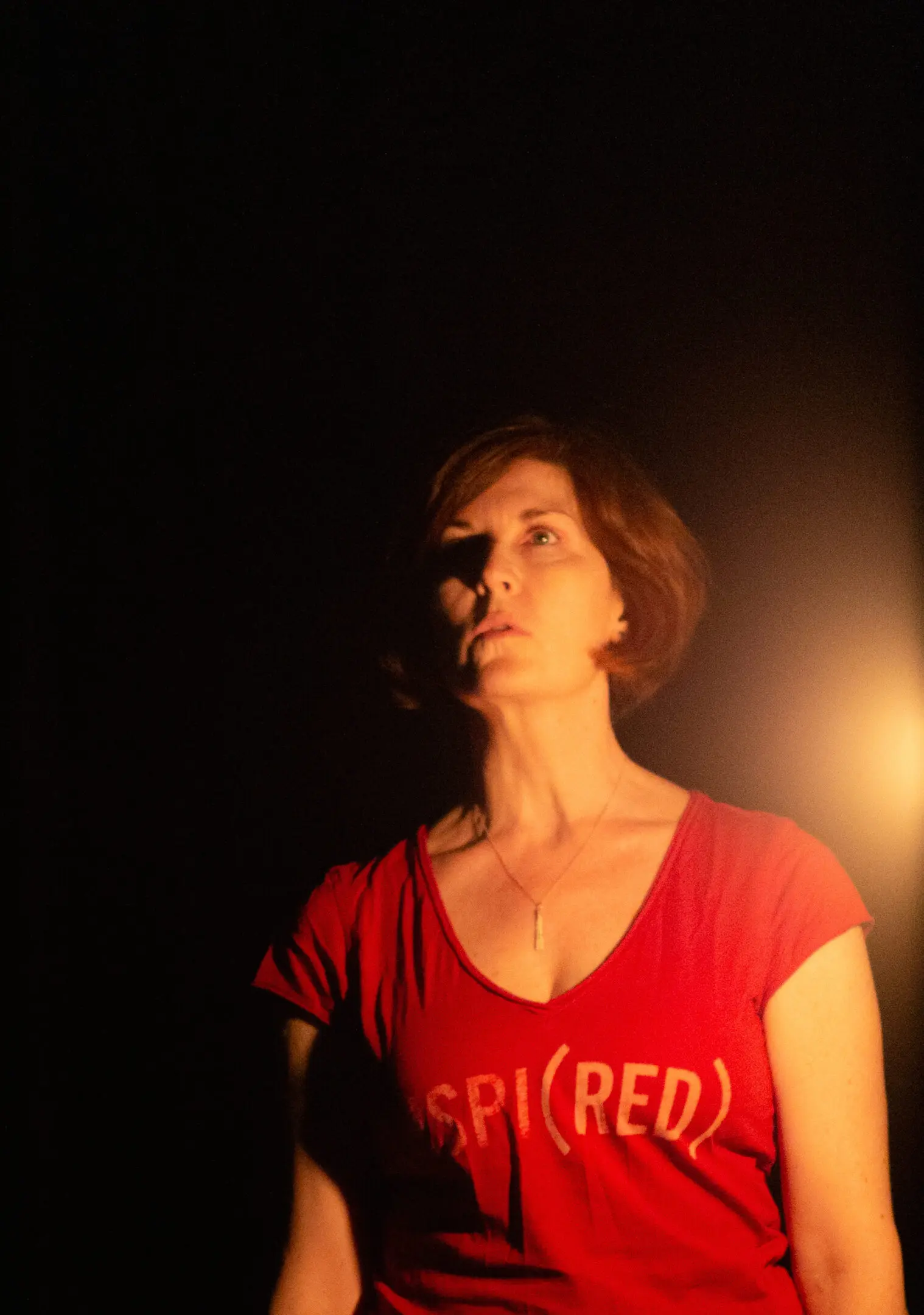 Woman in red shirt, dimly lit scene.