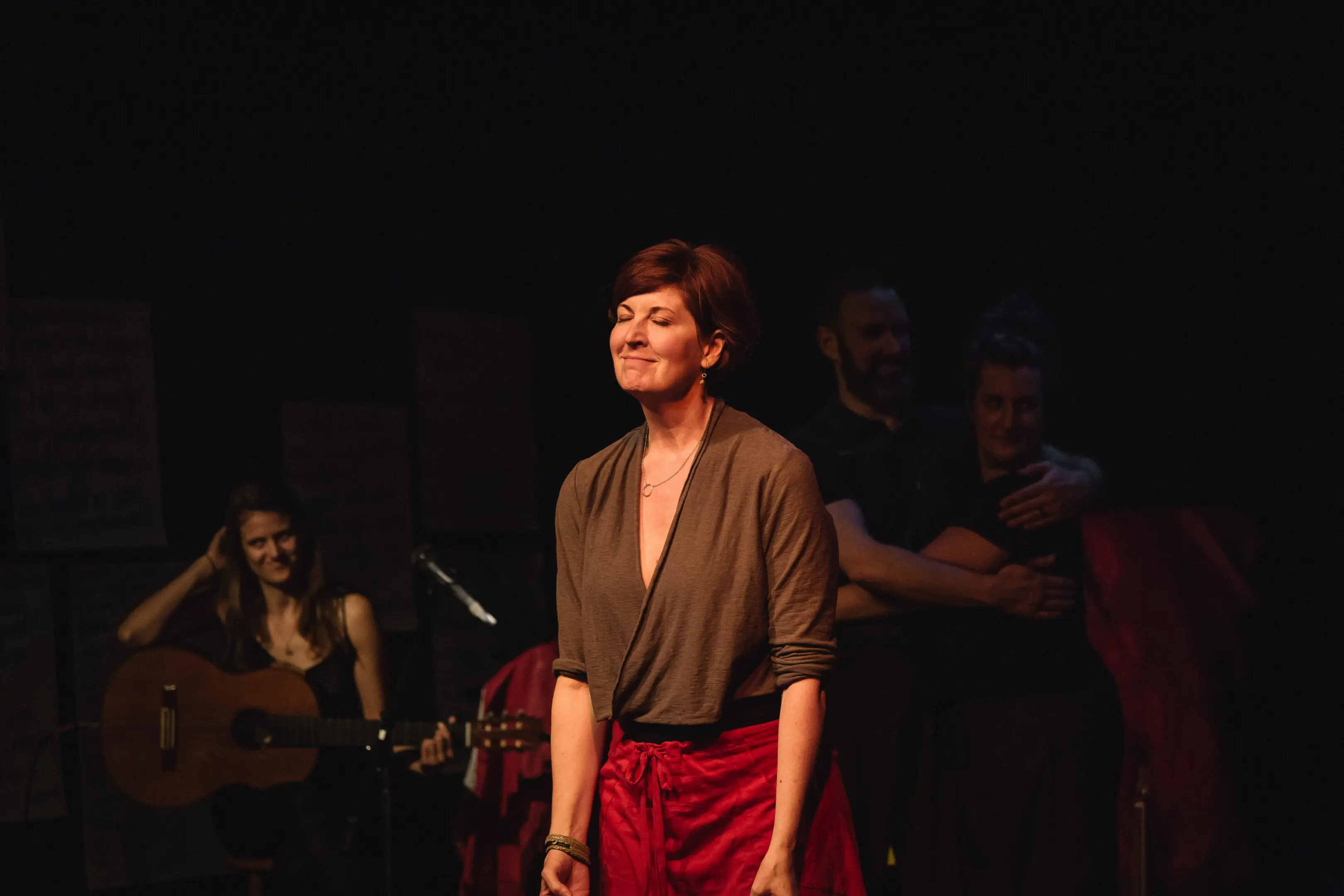Woman standing on stage with musicians behind.