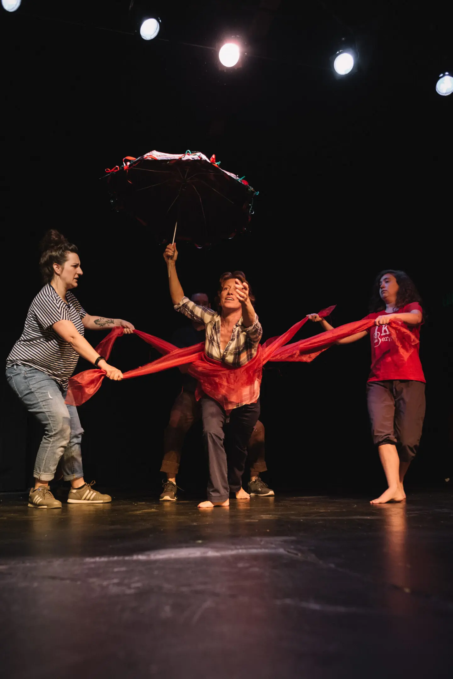 Performers with umbrella and red fabric on stage.