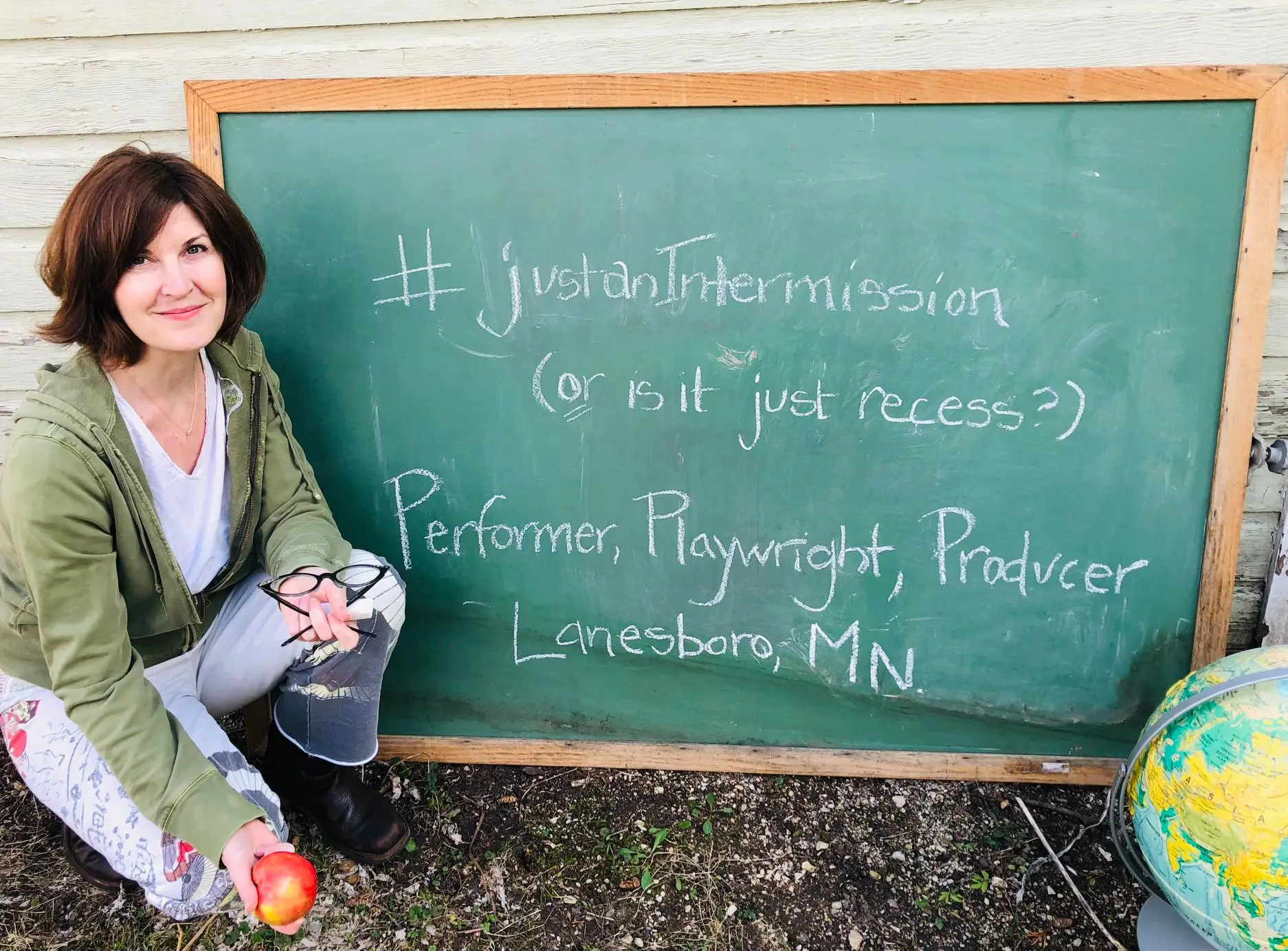 Woman sitting by chalkboard with apple.