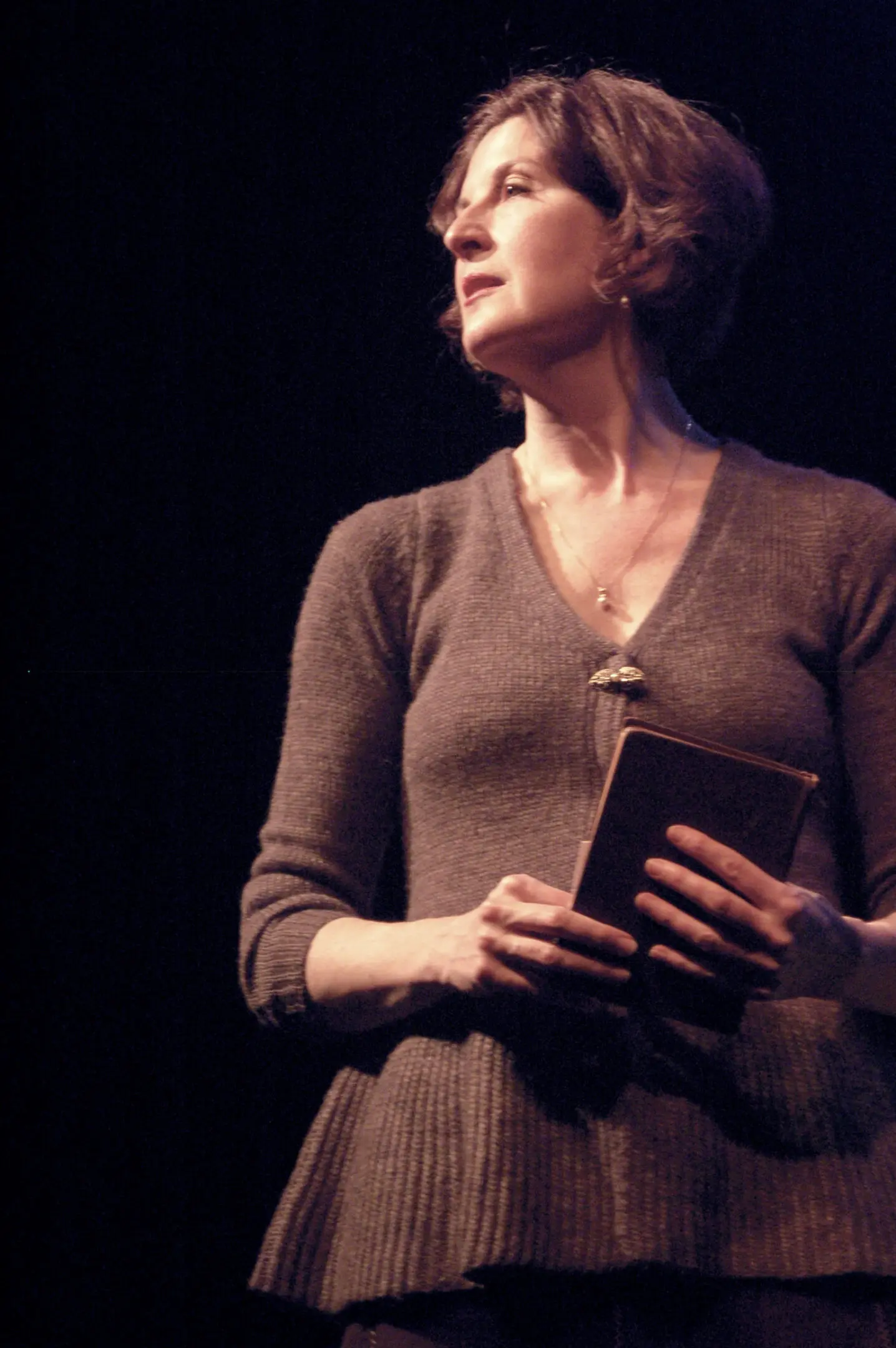 Woman holding a book on stage.