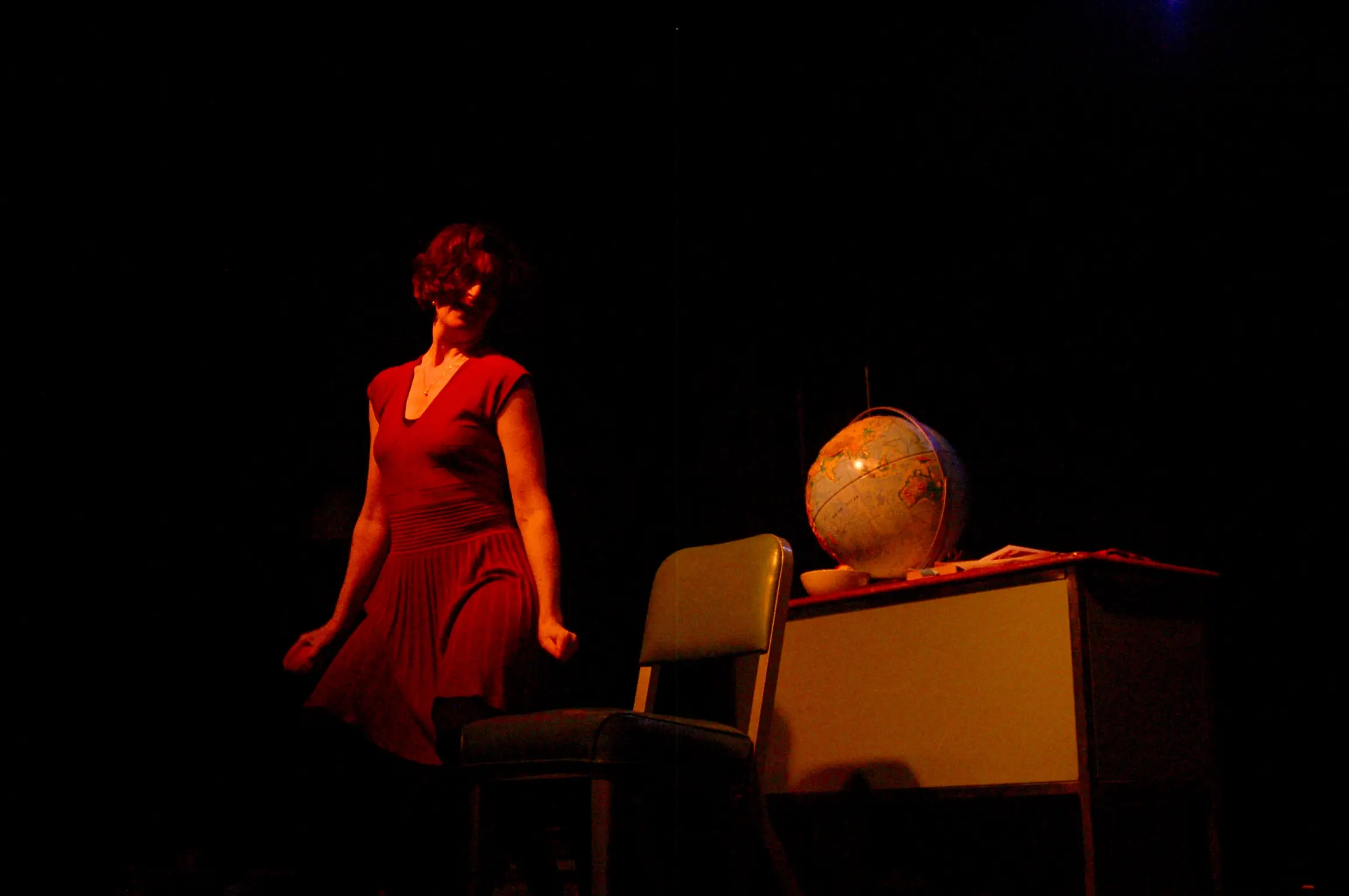 Woman performing beside desk with globe.