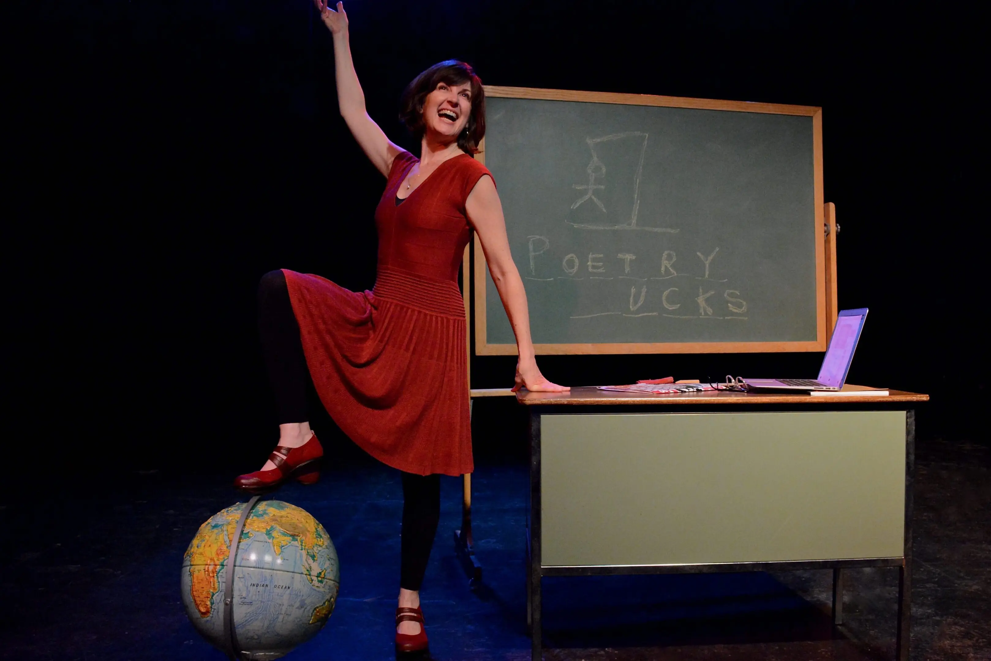 Woman posing with globe and classroom chalkboard.