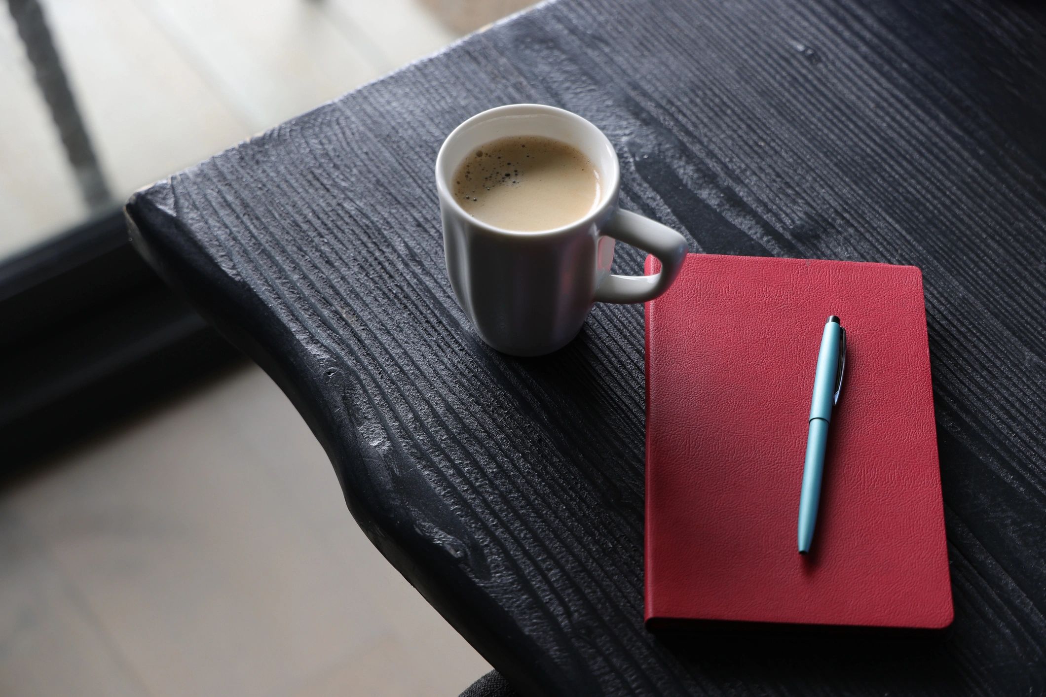 Red leather notebook with pen and coffee mug on black wooden desk